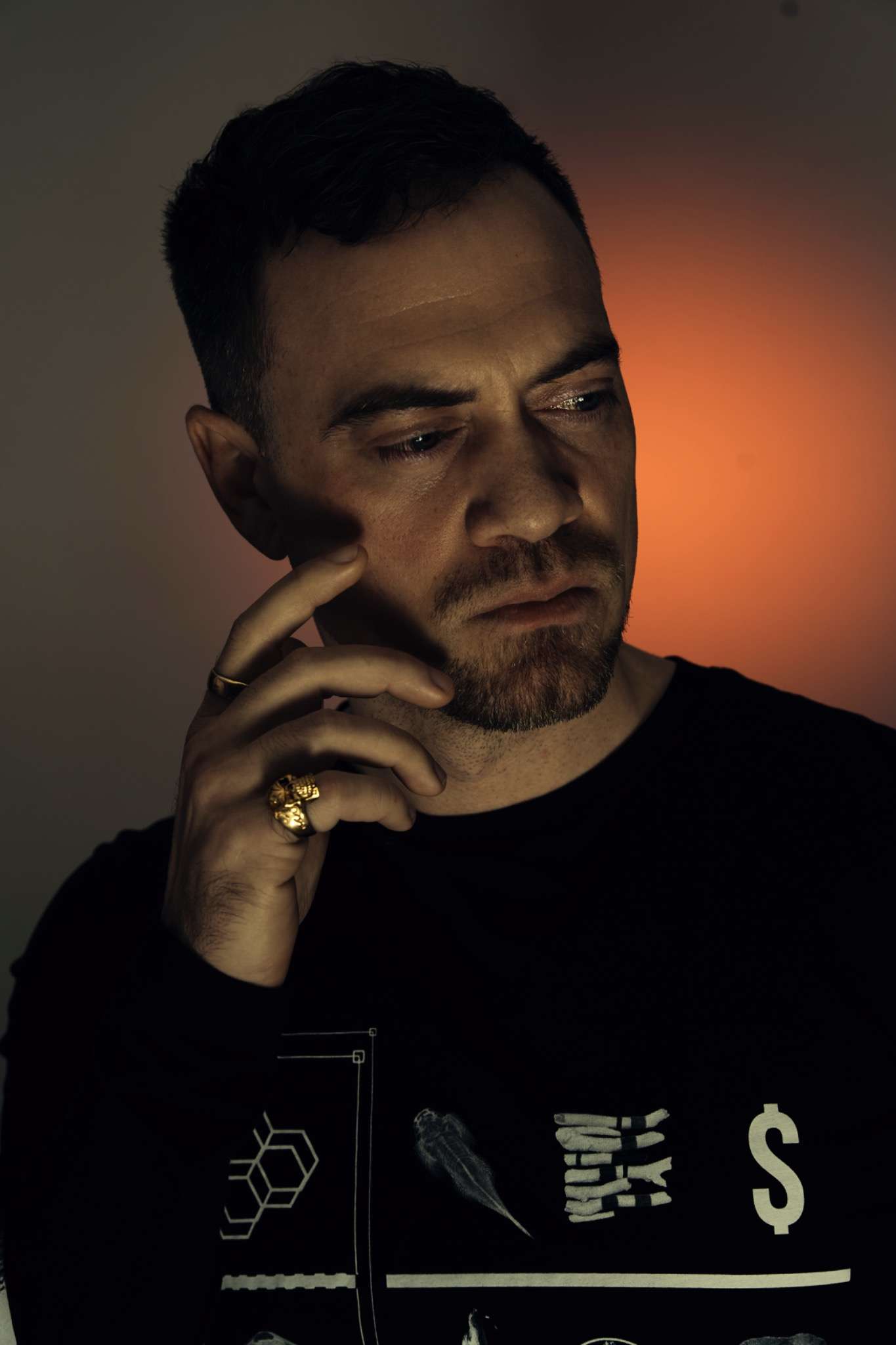 Anders Rath – the artist behind Voidcoloured – captured in a contemplative moment, wearing gold rings and black symbolic artwork.